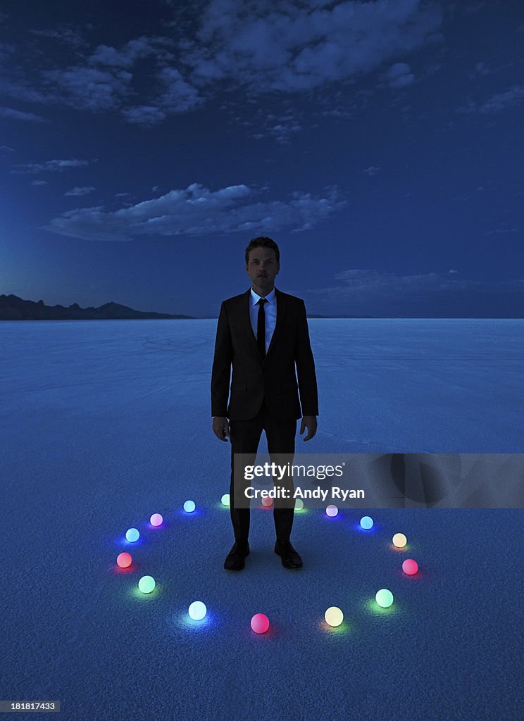 Man in circle of glowing orbs in desert at dusk.