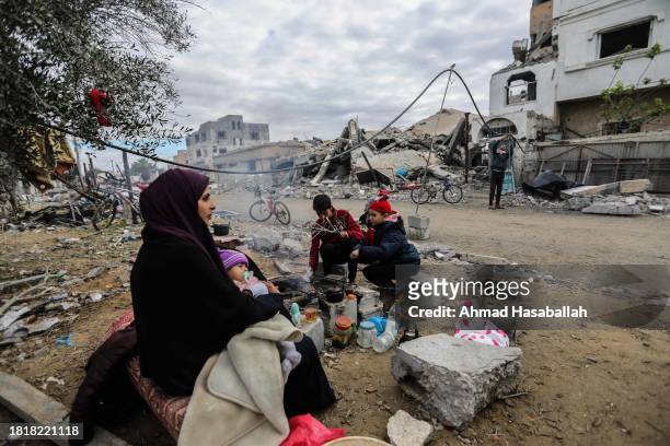 Family gathers around a fire in front of the rubble of their home, which was destroyed by air strikes in the Khuza’a area on November 28, 2023 in...