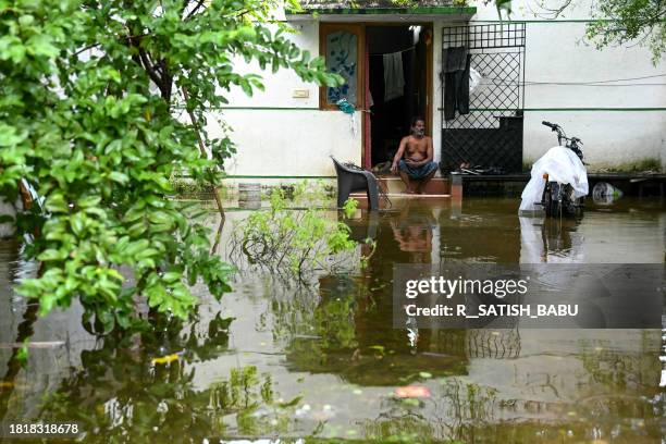 Man sits at his house in a flooded street after heavy rains ahead of Cyclone Michaung's landfall in Chennai on December 3, 2023.