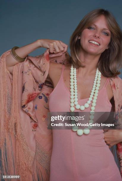 Portrait of American model and actress Cheryl Tiegs as she poses, dressed in a rose-colored, sleeveless dress, a pink, rose-patterned, fringed shawl,...