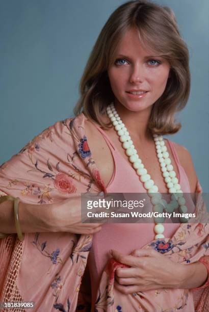 Portrait of American model and actress Cheryl Tiegs as she poses, dressed in a rose-colored, sleeveless dress, a pink, rose-patterned, fringed shawl,...