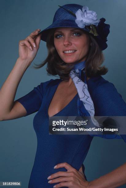 Portrait of American model and actress Cheryl Tiegs as she poses, dressed in a blue print neck scarf, a blue short sleeved V neck sweater, and a blue...