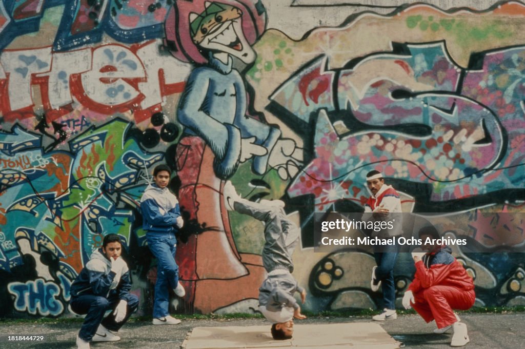 A group of young men demonstrate breakdancing in front of a wall ...