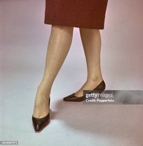 Posed close up studio portrait of the legs of a female fashion model wearing a red woollen skirt and kitten heeled black shoes, London, 14th October...