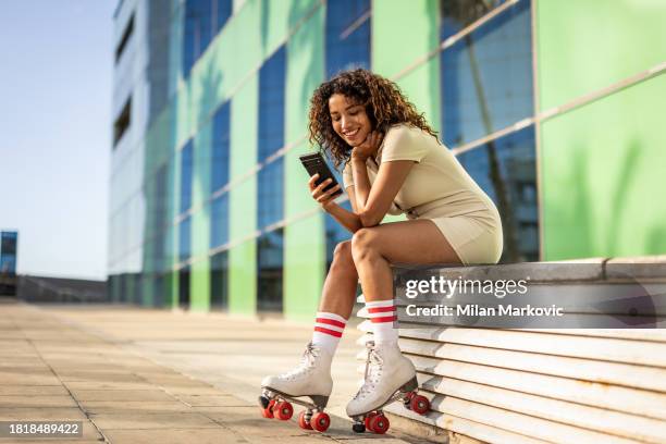 young beautiful spanish woman on roller skates during a summer day, resting next to a modern building in the city center - roller skates stock pictures, royalty-free photos & images