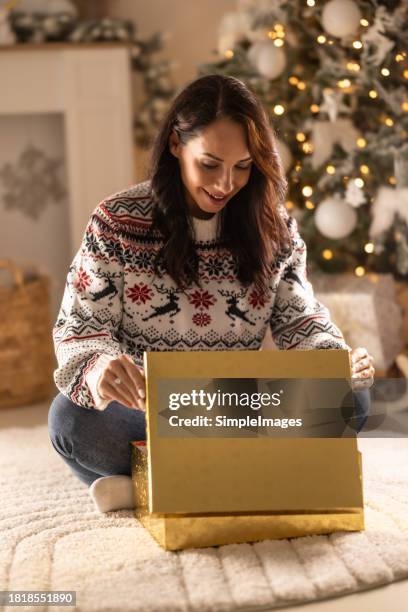 excited and surprised young caucasian woman smiles big as she opens a christmas gift and looks inside the plaid box. - big xmas stocking stock pictures, royalty-free photos & images