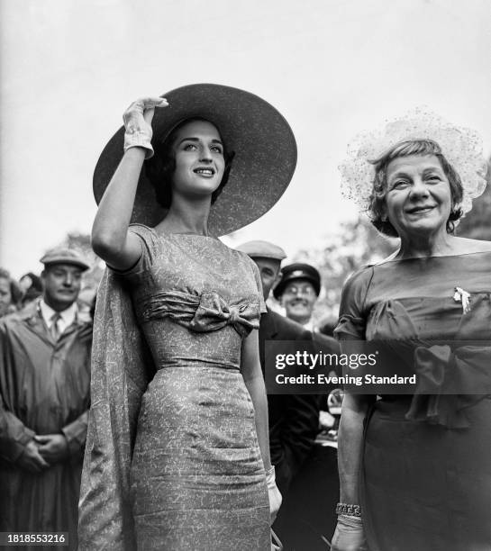 Two women racegoers, one wearing a caped dress and matching hat, attend the Royal Ascot race meeting, June 19th 1958.