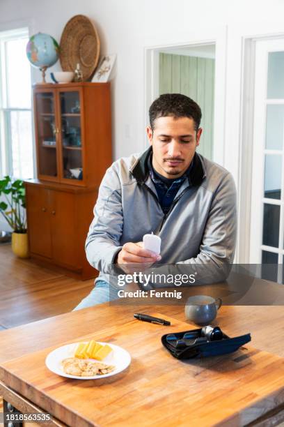 a multiracial mid adult man with diabetes reading his blood sugar levels on a glaucometer. - glaucometer stockfoto's en -beelden