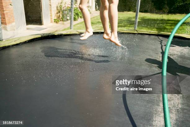 side view of the bare feet of two children jumping wet on a trampoline in the backyard of a house - bare feet kneeling girl stock-fotos und bilder