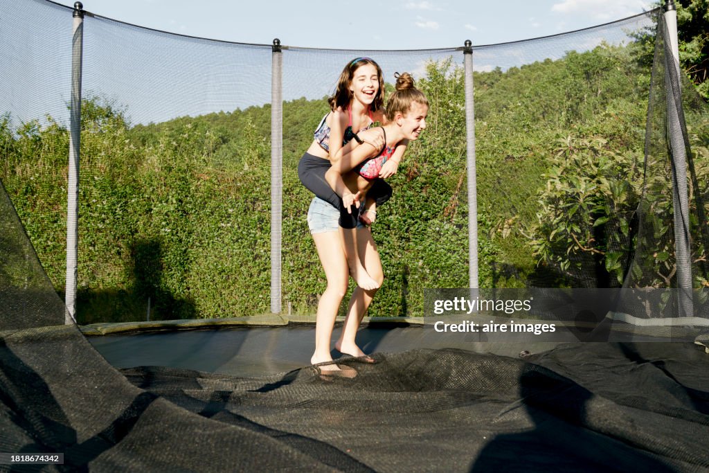 Two girls one carrying the other posing for the camera on a trampoline