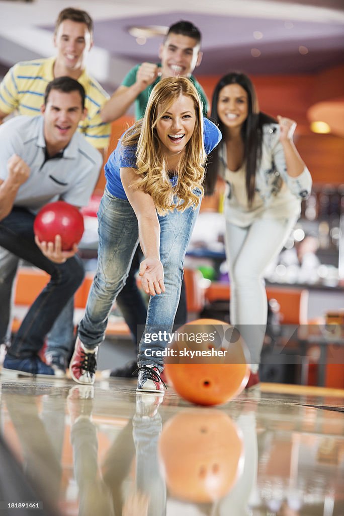 Friends cheering while girl is throwing a bowling ball