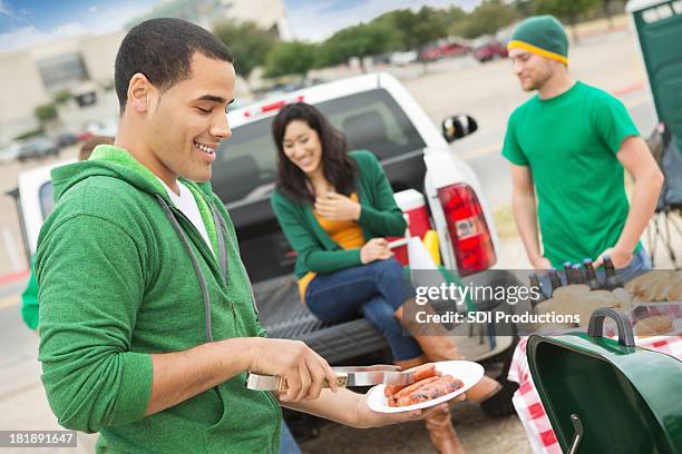 young man grilling during tailgating party near football stadium - football tailgate stock pictures, royalty-free photos & images