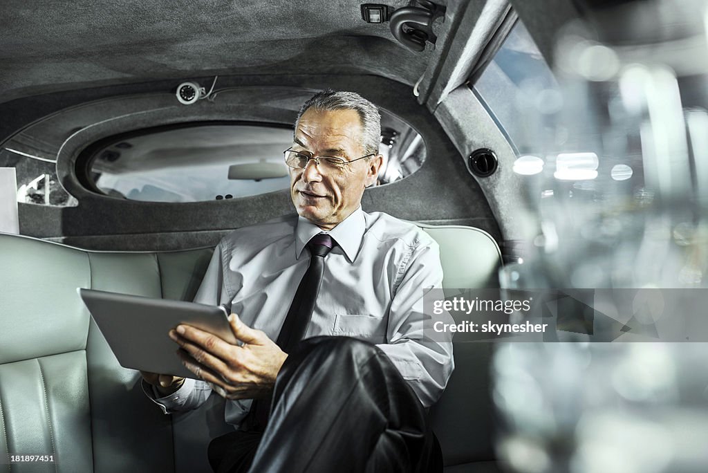 Mature adult businessman working on digital tablet in limousine.
