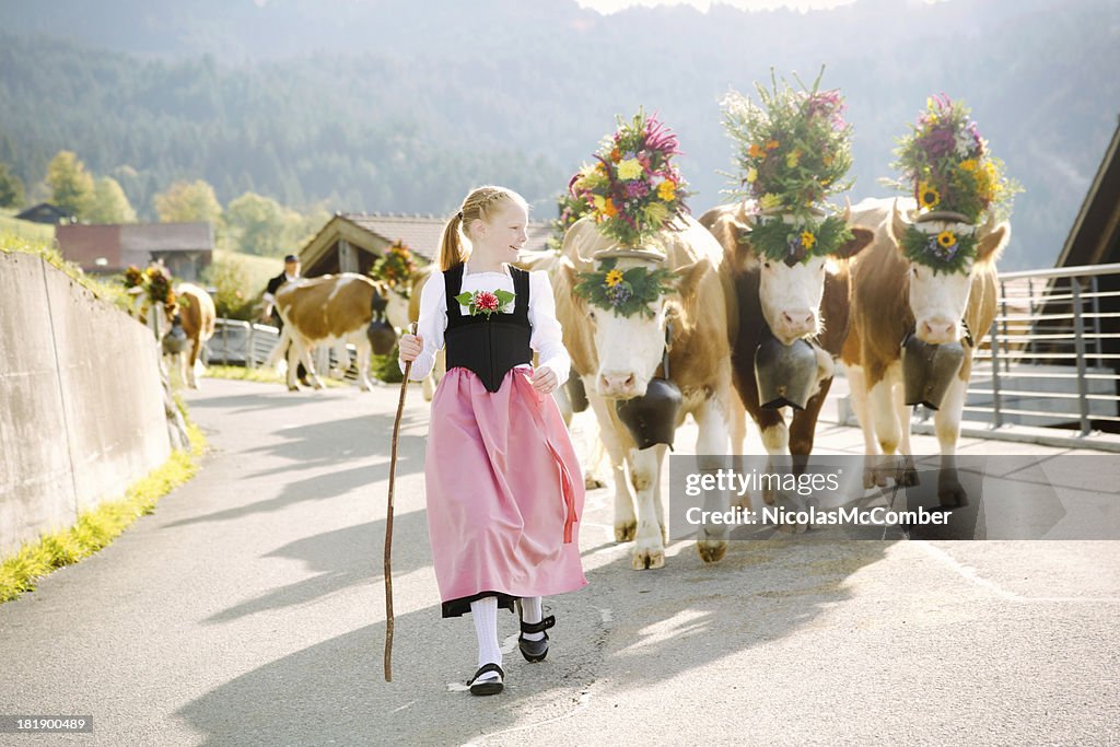 Young Swiss farmer girl leading decorated cows to fair