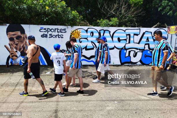 Fans of Gremio walk by a mural painting depicting Uruguayan striker Luis Suarez on their way to the Brazilian Championship football match between...