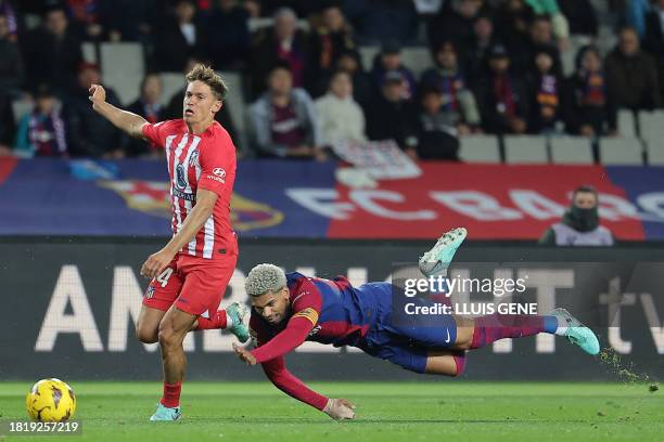 Barcelona's Uruguayan defender Ronald Araujo falls down as he challenges Atletico Madrid's Spanish midfielder Marcos Llorente during the Spanish...