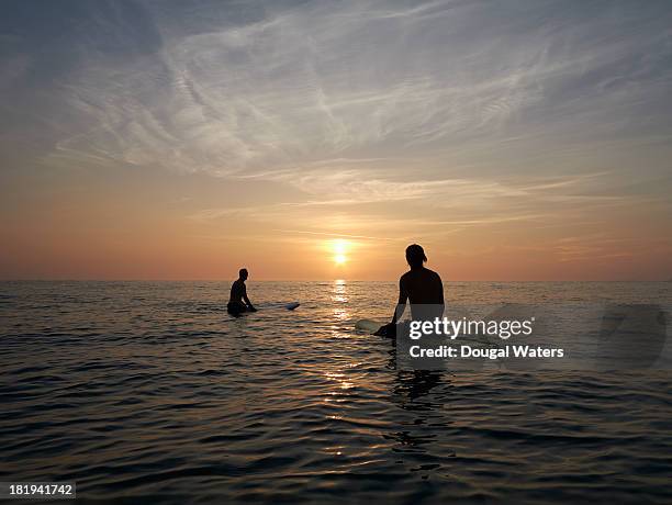 surfers sitting on boards at sunset. - sitting in water stock pictures, royalty-free photos & images