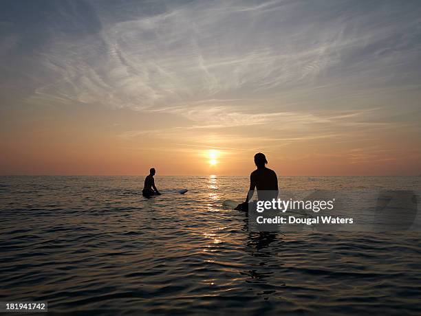 surfers sitting on boards at sunset. - surfers in the sea at sunset stock pictures, royalty-free photos & images