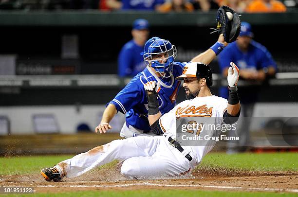 Nick Markakis of the Baltimore Orioles scores in the third inning ahead of the throw to J.J. Arencibia of the Toronto Blue Jays at Oriole Park at...