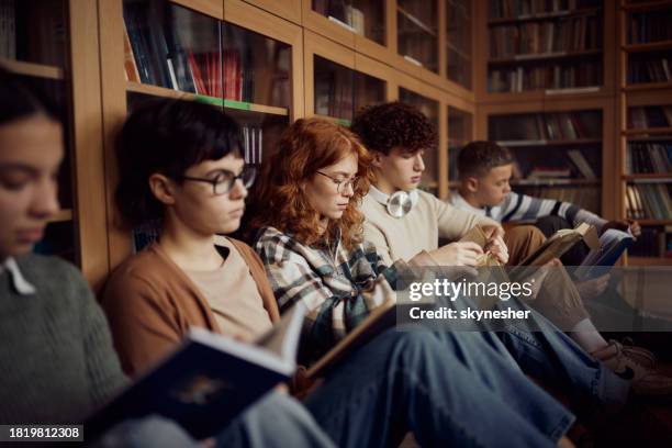 group of students reading books on floor in library. - literature stock pictures, royalty-free photos & images