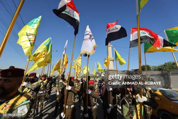 Fighters lift flags of Iraq and paramilitary groups, including al-Nujaba and Kataib Hezbollah, during a funeral in Baghdad for five militants killed...