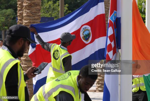 Workers hoist flags, including that of Costa Rica, of nations participating in the UNFCCC COP28 Climate Conference the day before its official...