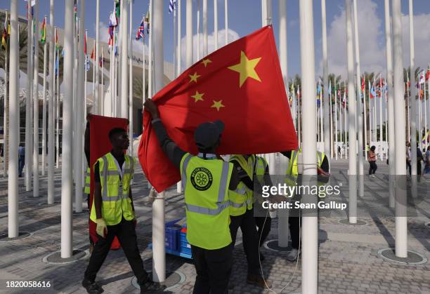 Workers hoist flags, including that of China, of nations participating in the UNFCCC COP28 Climate Conference the day before its official opening on...
