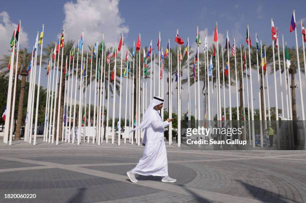 Man wearing a thawb walks past flags of nations participating in the UNFCCC COP28 Climate Conference the day before its official opening on November...