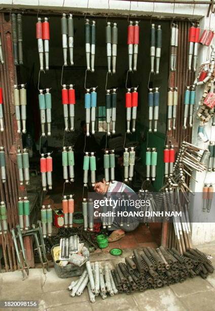 Man sits working behind a curtain of motorcycle shock-absorbers hung in his workshop doorway in a Hanoi street 09 April. There is a great demand for...