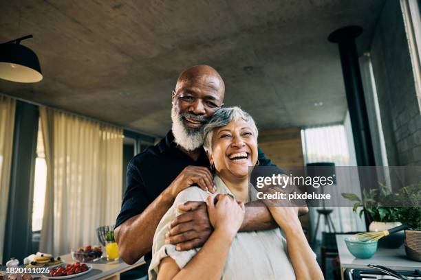 pareja afroamericana jubilada activa que comparte una risa en la cocina de una casa moderna - black couple married fotografías e imágenes de stock