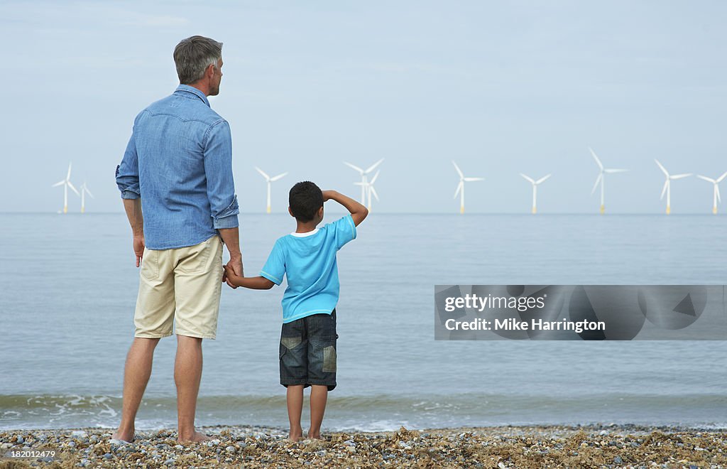 Father and son on beach looking at wind farm.