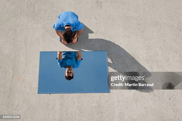 man kneeling on ground with mirror and reflection - 浮華 個照片及圖片檔