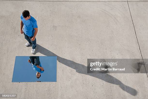 mann stehend mit spiegel auf boden und reflexion - reflexion stock-fotos und bilder