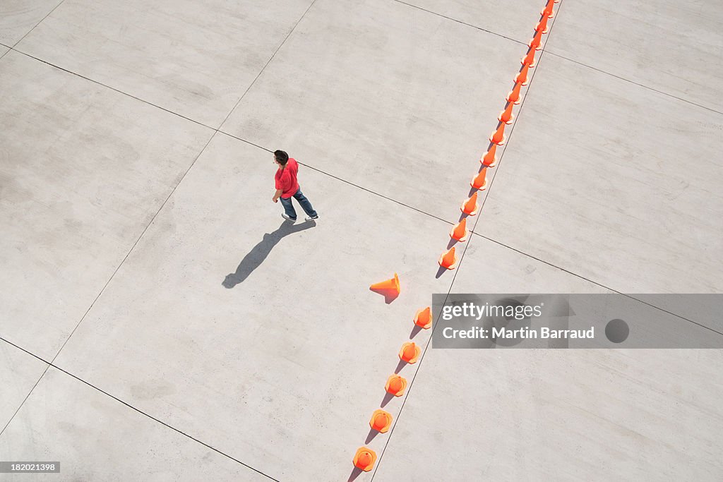 Man walking away from row of traffic cones with one misplaced