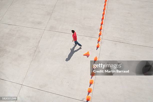 man walking away from row of traffic cones with one misplaced - person standing far stockfoto's en -beelden