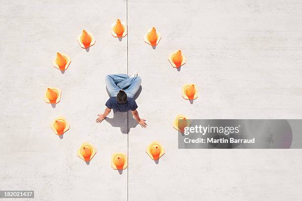 man sitting down in circle of traffic cones with arms up - pylons stockfoto's en -beelden