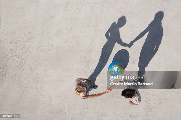 aerial view of two people shaking hands with shadow and globe outdoors - international day two stock pictures, royalty-free photos & images