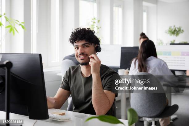 man wearing headset using desktop pc in office - arab call center stock pictures, royalty-free photos & images