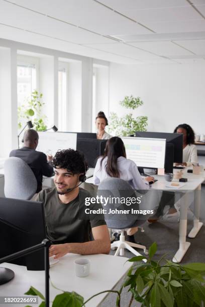 man wearing headset using desktop pc in office - arab call center stock pictures, royalty-free photos & images