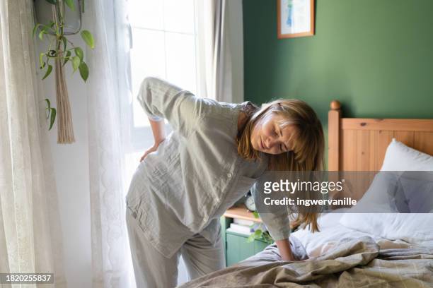 grimacing woman suffering from pain in back leaning against bed - emirati lady from back stock-fotos und bilder