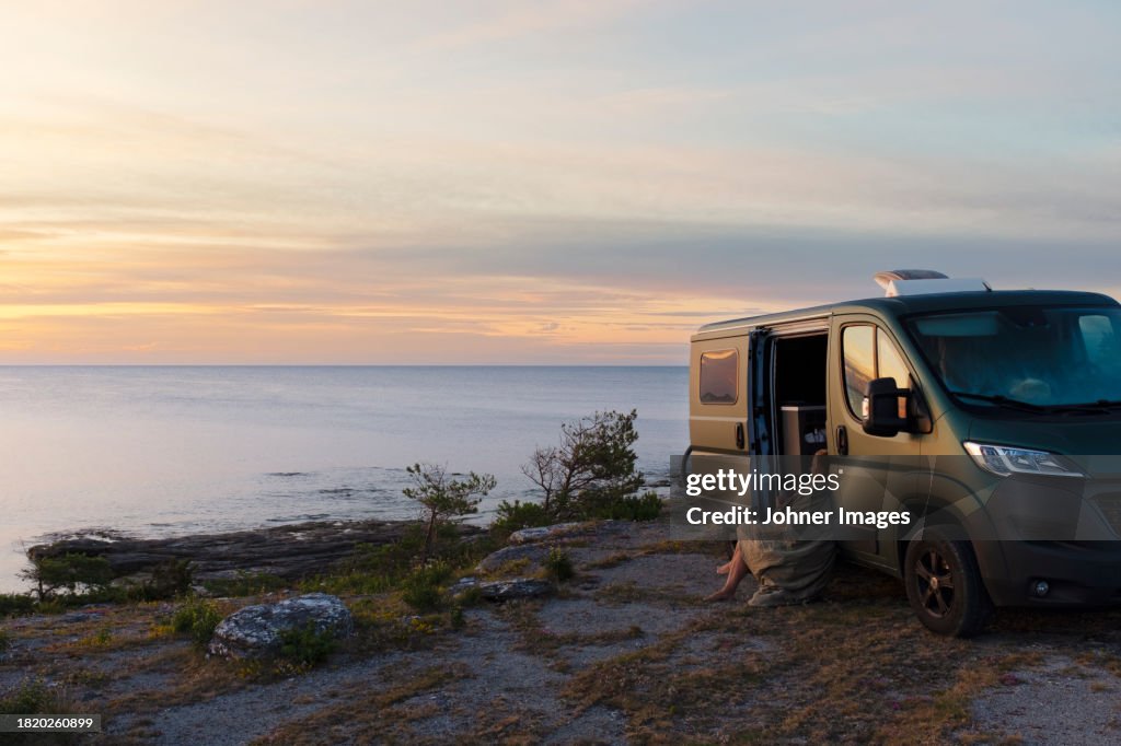 Woman sitting near motorhome and looking at sea