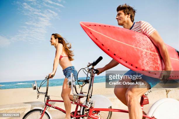 couple riding bikes on beach boardwalk - bike beach stockfoto's en -beelden