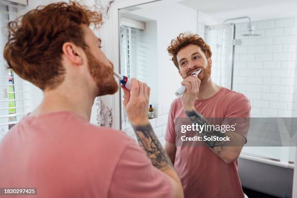 brushing teeth in the mirror - electric toothbrush stock pictures, royalty-free photos & images