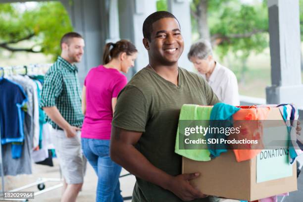 man holding box of clothes donations at a donation center - man holding donation box stock pictures, royalty-free photos & images
