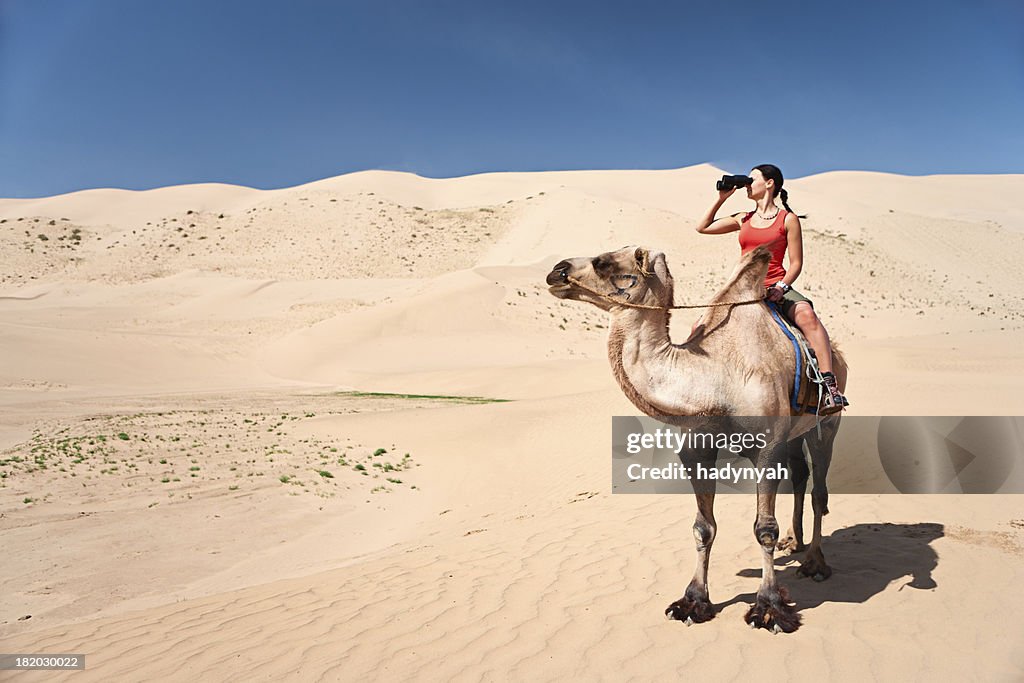 Young woman is looking through a binoculars on the camel