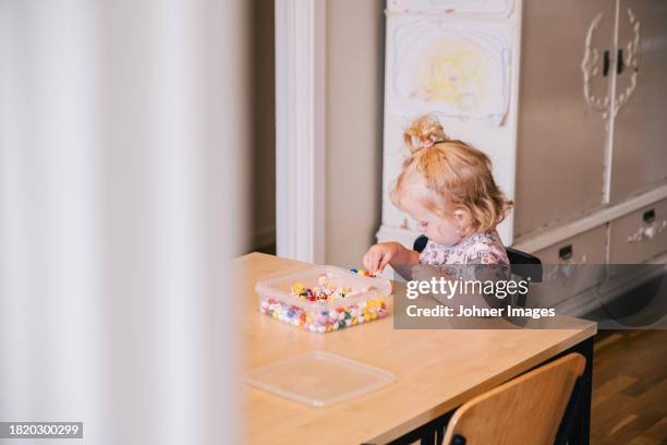 blond girl playing with beads on table at home - white bead stock pictures, royalty-free photos & images