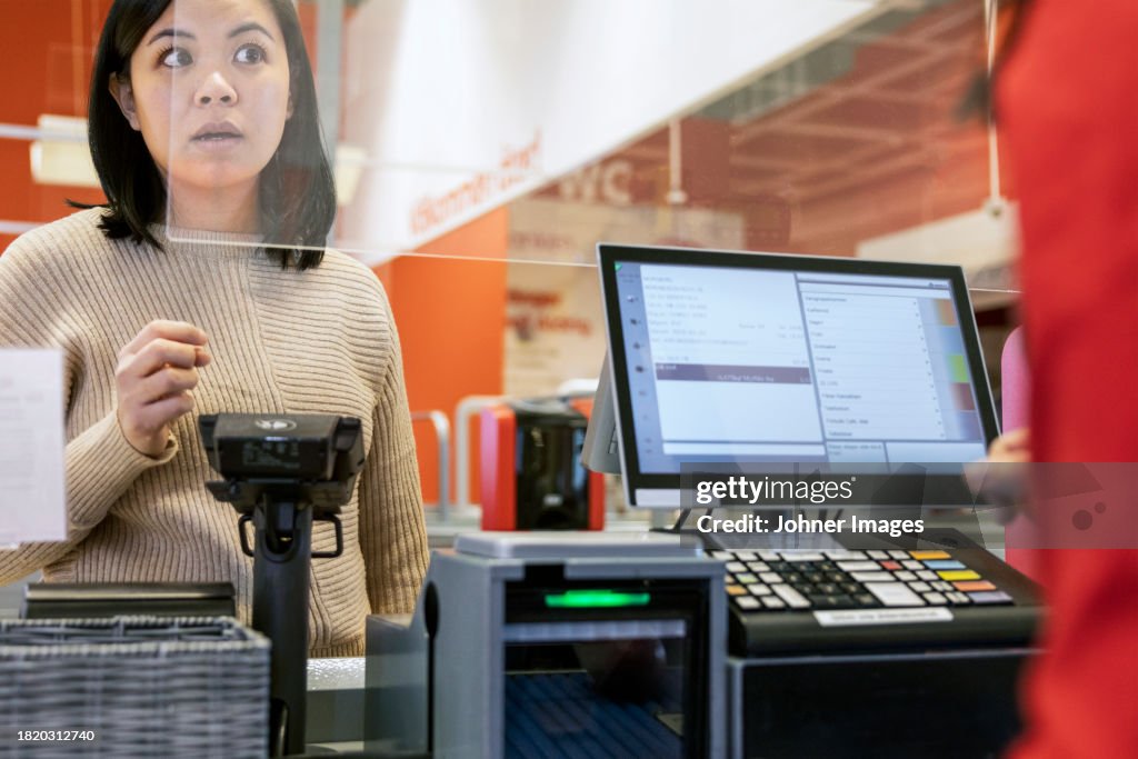 Young female customer talking to cashier at checkout in supermarket