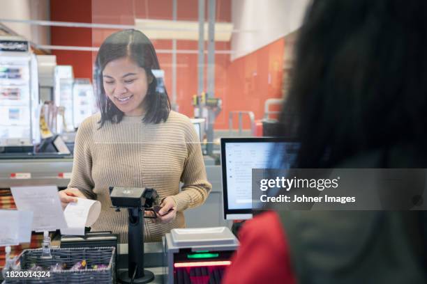 smiling young female customer taking receipt at checkout in supermarket - receipt stock pictures, royalty-free photos & images