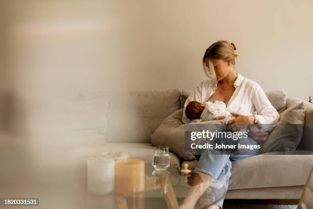 mother breastfeeding son while sitting on sofa at home - breastfeeding stock pictures, royalty-free photos & images