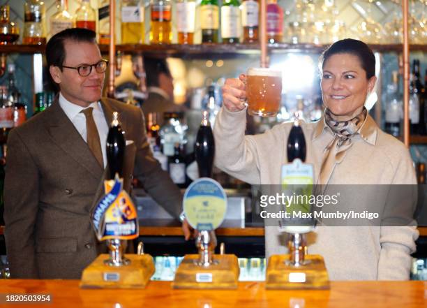 Prince Daniel of Sweden looks on as Crown Princess Victoria of Sweden pulls a pint of beer as they visit the Three Blackbirds Pub, Woodditton to meet...